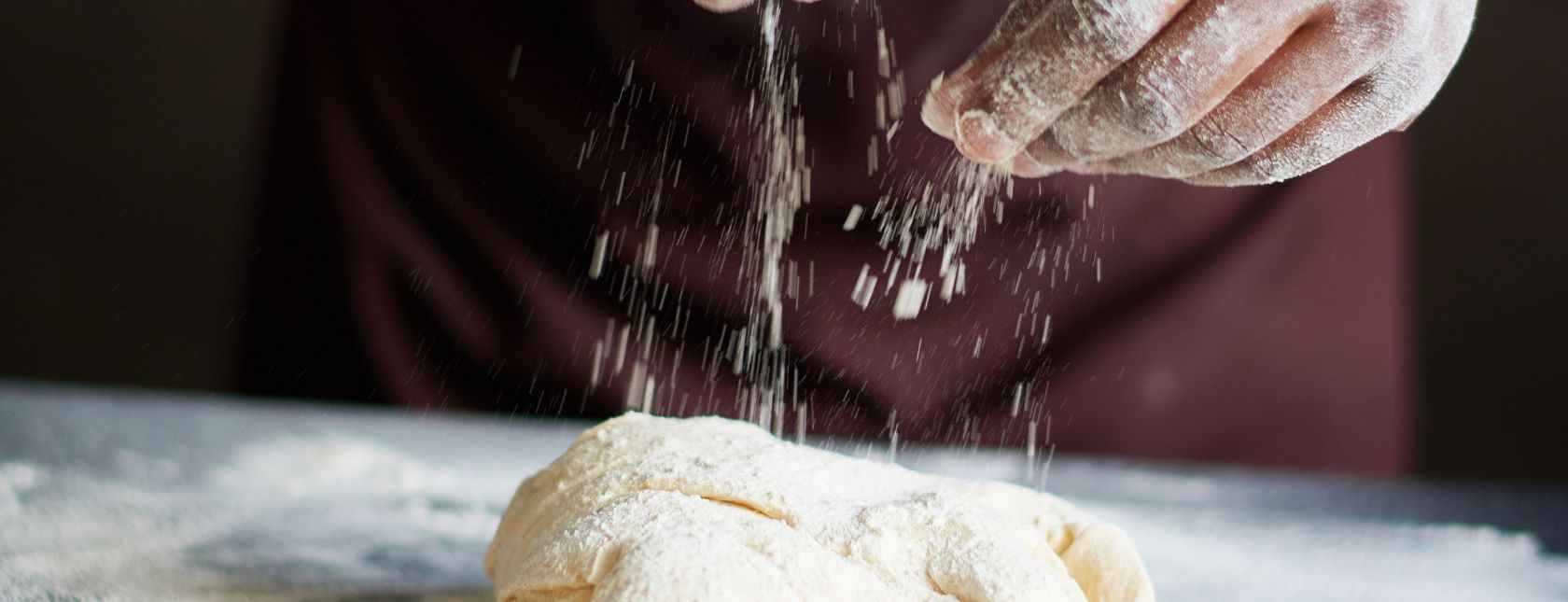 Baker sprinkling flour onto kneaded dough